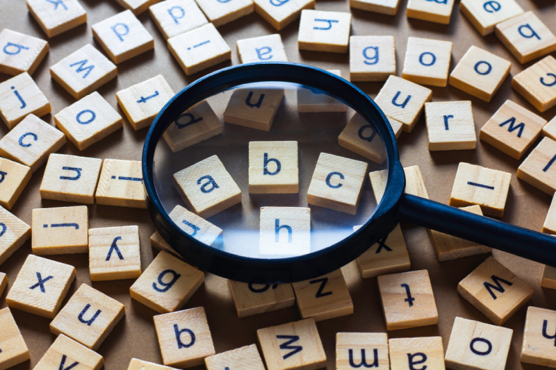 Lupa powiększająca drewniane literki – symbol poszukiwania fraz kluczowych w kampaniach Paid Search i Paid Social.