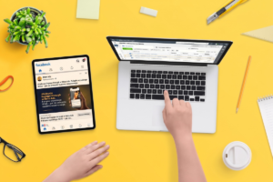 Biurko na żółtym tle z laptopem wyświetlającym panel Meta Ads Manager oraz tabletem z podglądem reklamy na Facebooku dotyczącej atrybucji Engage-through w Meta Ads
